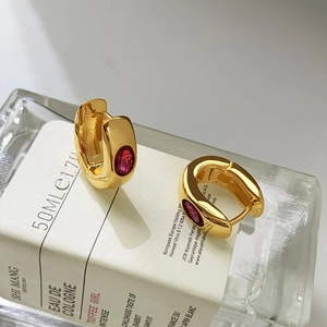French vintage gold hoop earrings with green zircon inlay on a white glass bottle
