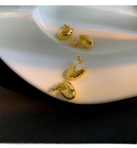 Vista macro di orecchini a perno ovali dorati lucidi su un piatto in ceramica bianca