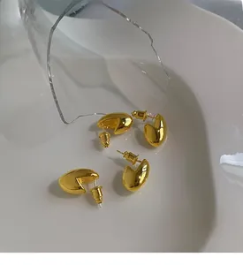 Dettaglio di orecchini a lobo ovali dorati lucidi su un piatto di ceramica minimale