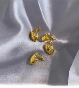 Dettaglio di orecchini a bottone dorati su un elegante tessuto di seta grigia