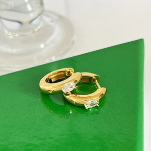 Macro view of gold hoop earrings with central oval zircon on a geometric green stand