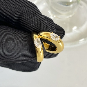 Detail of gold chunky hoop earrings with oval zircon stones held by a gloved hand