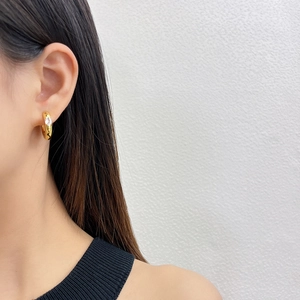Close-up of elegant gold hoop earrings featuring a drop-shaped zircon on a model