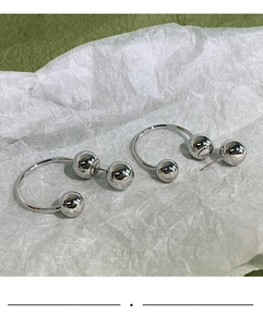 Detail of minimalist silver-finish U-shaped earrings with dual polished metal spheres