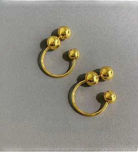 Detailed view of gold C-shaped earrings with solid metal balls on a leather surface