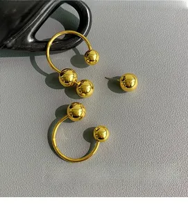 Macro shot of minimalist gold spherical earrings on a textured grey leather surface