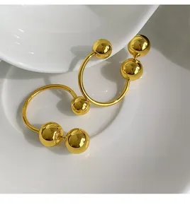 Detailed view of gold C-shaped earrings with three polished metal spheres on ceramic