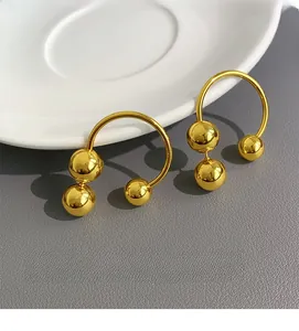 Macro shot of gold geometric earrings with ball accents on a grey textured background