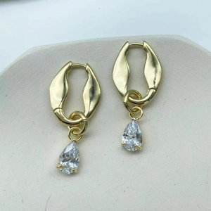 Elegant gold teardrop earrings with sparkling zircon pendant on a textured stone surface