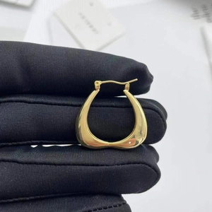 Polished gold geometric heart earrings held by a gloved hand on a white background