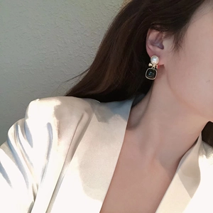Vintage style gold earrings featuring a white pearl and green gemstone drop on a model