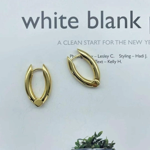 Elegant gold oval metal hoop earrings with round drop detail on a magazine backdrop