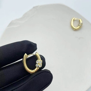 Boucles d'oreilles en U dorées avec trèfle en zircon tenues par une main gantée de noir