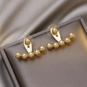 Close-up of golden fan-shaped brass ball earrings on premium silk and jewelry box