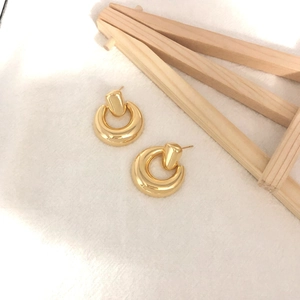 Detailaufnahme klobiger goldener geometrischer Creolen auf strukturiertem Stoff und Holz