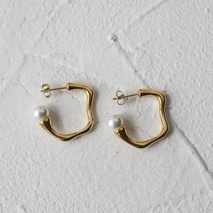 Détail de boucles d'oreilles vagues dorées avec perles sur fond de marbre blanc texturé