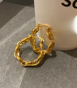 Close-up of gold pig-nose chain earrings hanging on a white mug with polished finish