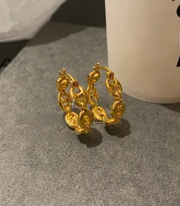 Macro shot of 18K gold coffee bean link hoop earrings on a textured grey surface