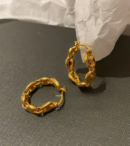 Detailed view of golden marina chain link hoop earrings on a textured background