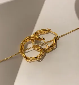 Macro detail of polished gold-plated mariner link earrings on a white wavy stand