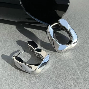 Polished silver chunky U-shaped geometric hoop earrings on a textured luxury background