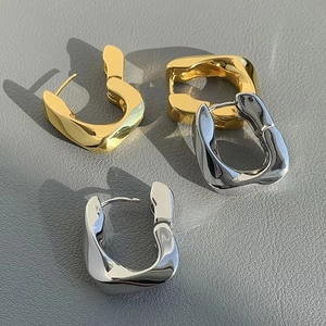 Close-up of gold and silver U-shaped chunky hoop earrings on grey leather surface