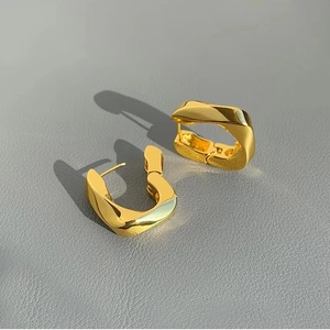 Macro shot of polished gold geometric U-shaped hoop earrings on grey leather surface