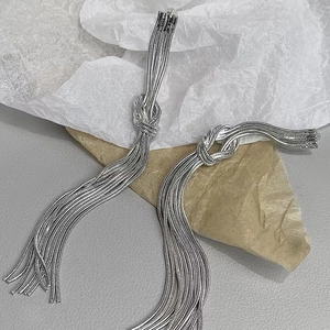 Silver snake chain tassel drop earrings with knot design on textured paper backdrop