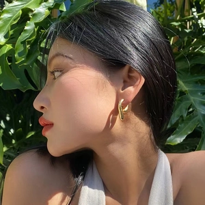 Fashion gold plated cross C-shaped earrings worn by a model against green leaves