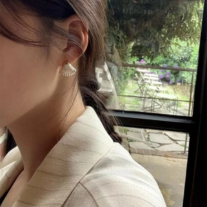 Shell shaped silver metal stud earrings with textured finish worn on ear lobe