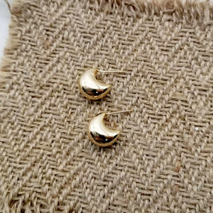 Detailed close-up of polished gold croissant dome earrings on a textured fabric surface