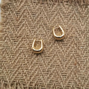 Detail of elegant gold U-shaped hoop earrings on textured brown fabric background
