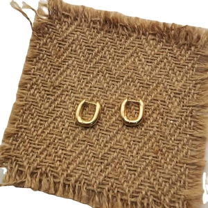 Elegant gold U-shaped huggie earrings with polished finish on rustic burlap base
