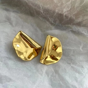 Vue détaillée de boucles d'oreilles dorées irrégulières sur un fond texturé délicat