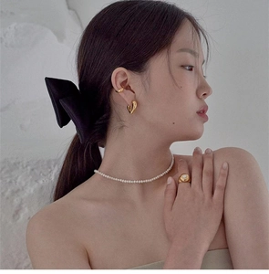 Elegant gold heart earrings and pearl necklace jewelry styled on model with a black bow