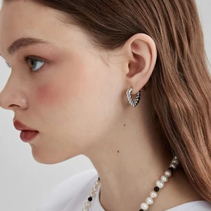 Detailed view of silver twisted rope C-shaped hoop earring on model with pearl necklace