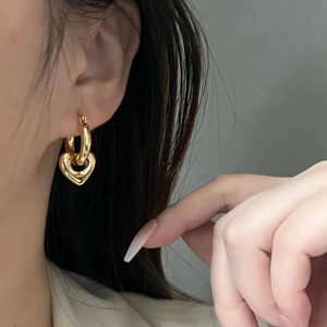 Polished gold-plated heart pendant hoop earrings worn by a model in a close-up shot