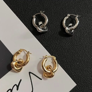 Detail of interlocking heart pendants on gold and silver hoops over a textured background