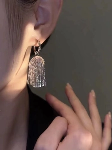 Detail of silver tassel earrings with long metal strands in sunset light on model