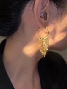 Detailed view of elegant gold metal tassel earrings worn by a model in warm light