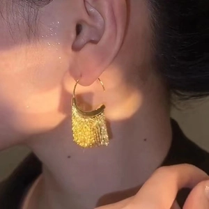 Elegant gold tassel earrings with metallic fringes shown on model under warm lighting
