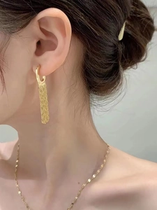 Close-up of elegant gold tassel hoop earrings and fine chain necklace on a model