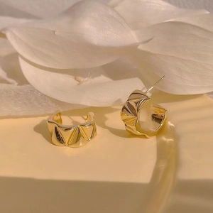 Detail of gold C-shaped earrings with geometric textured finish on a minimalist background