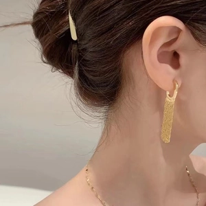 Elegant gold-tone rectangle drop earrings with textured finish shown on a female model