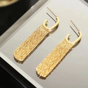 Elegant gold metal tassel earrings with C-shaped hooks shown on a reflective surface