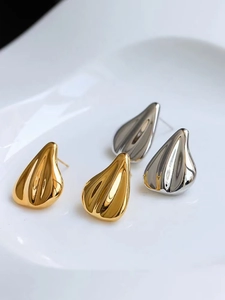 Detail of teardrop earrings featuring ribbed metallic texture in gold and silver finish