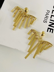 Macro shot of gold tassel pine needle earrings on white leather textured background