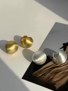 Detail of matte brushed metal ball earrings in gold and silver finish with elegant shadows