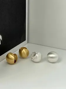 Detailed view of matte brushed spherical stud earrings in gold and silver finishes
