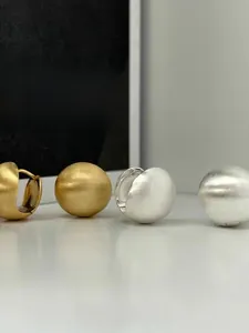 Macro detail of brushed matte texture on gold and silver spherical hoop earrings